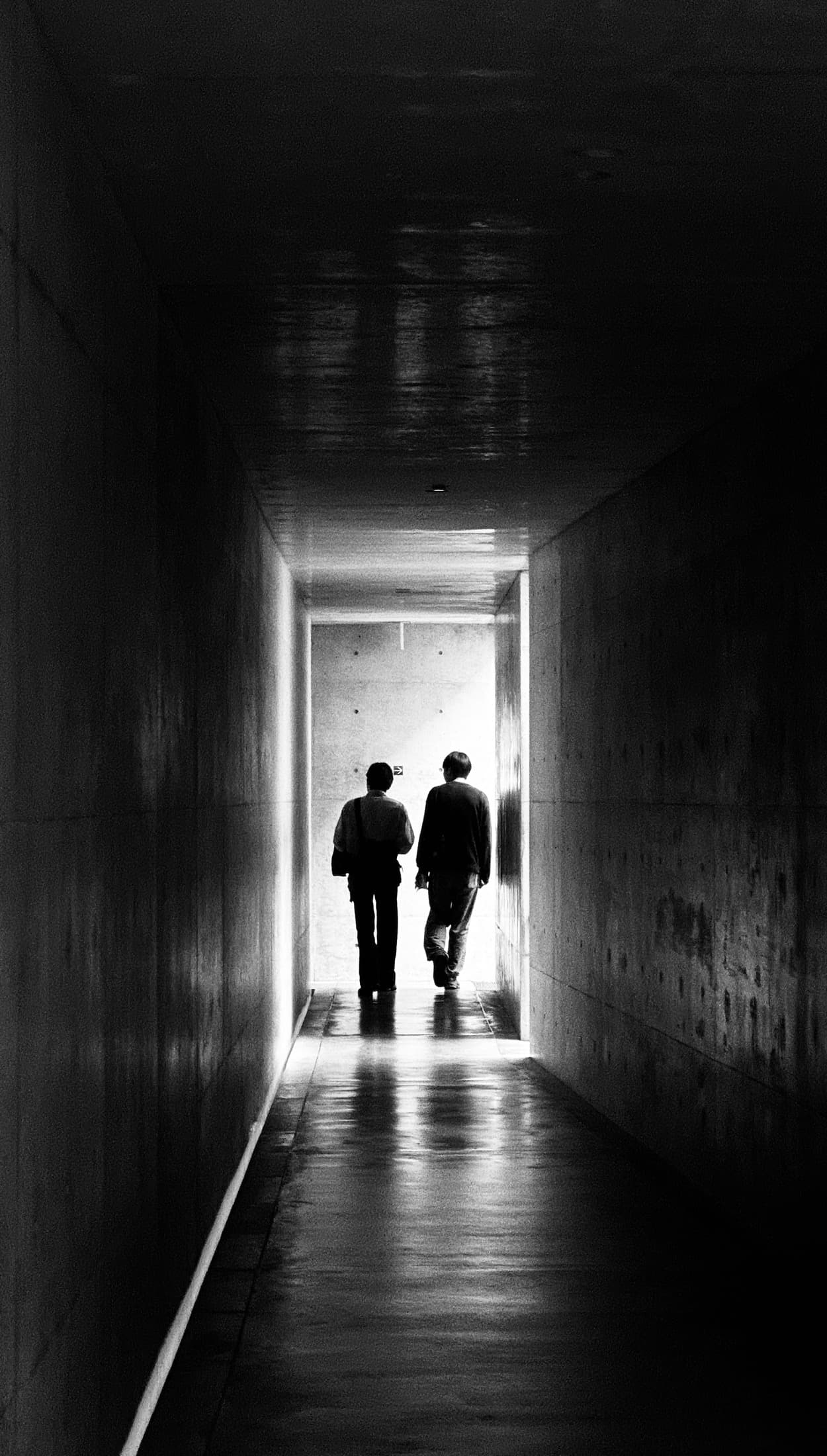 Two people walking through a dark concrete passage